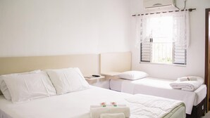 A hotel room with a large bed, a smaller bed, a nightstand, a window with curtains, and an air conditioning unit. - Hotel Guaíba (Guaiba)