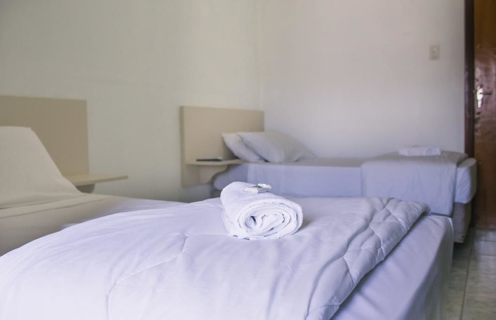 A hotel room with two beds, each with a pillow and a rolled towel.