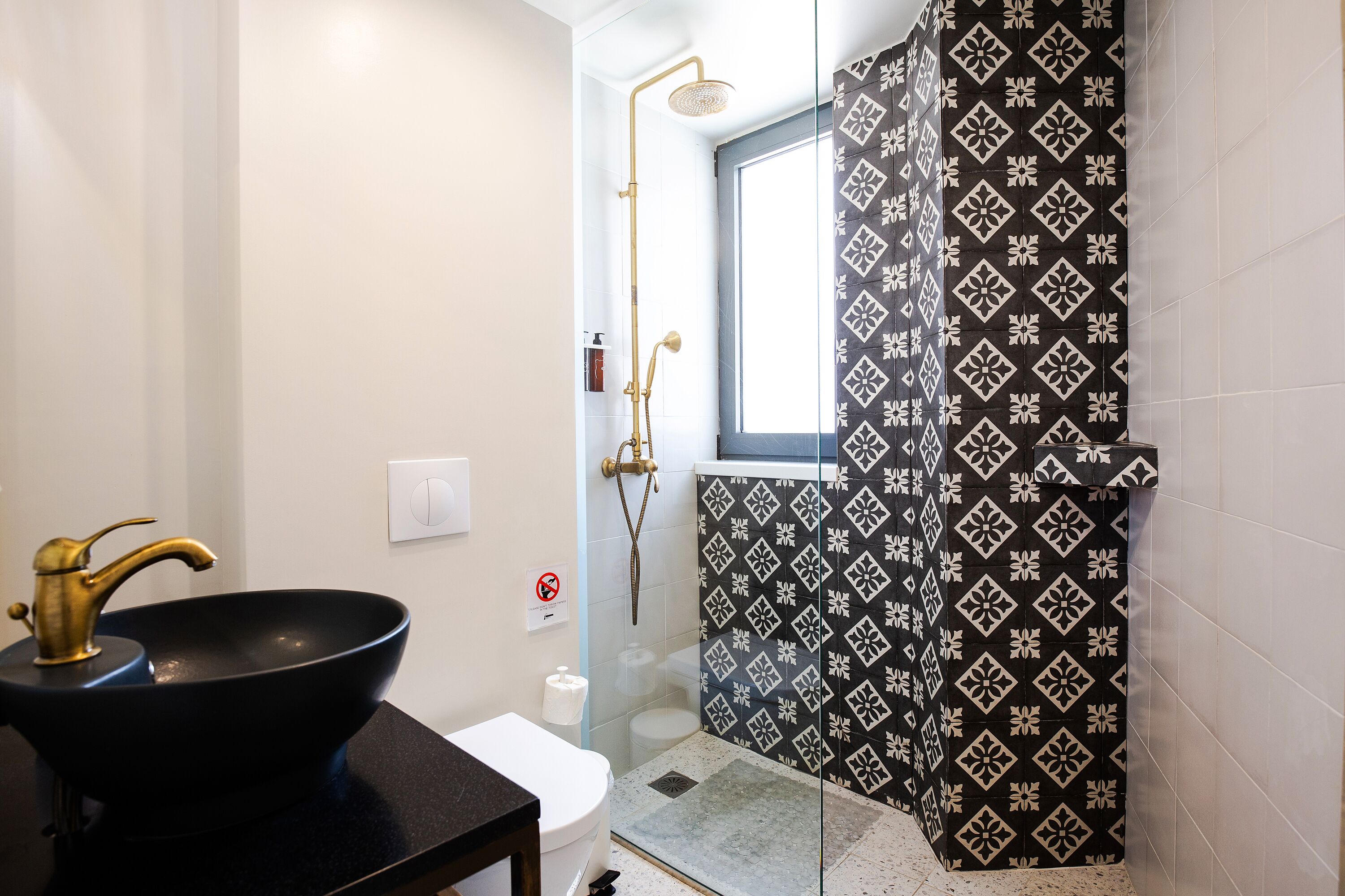 Un baño con un lavamanos negro, inodoro blanco y una ducha con cortina estampada.