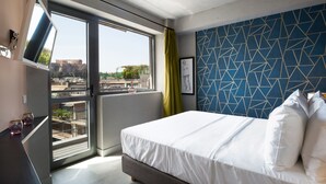 Ein Hotelzimmer mit Bett, Fernseher und einem Fenster mit Blick auf Gebäude.