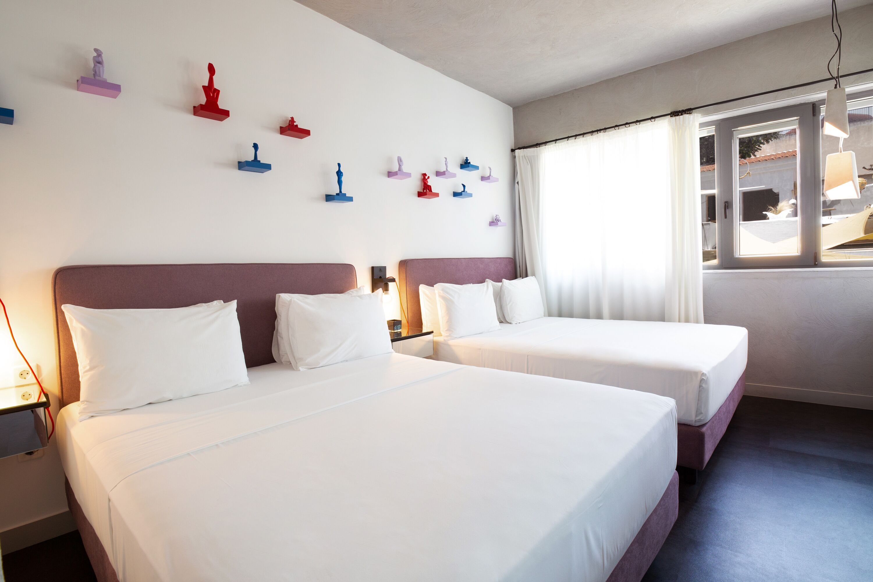 A hotel room with two beds, a window with curtains, and wall-mounted decorative items.
