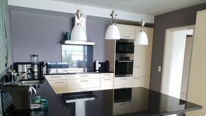 Une cuisine moderne avec un plan de travail noir, des meubles blancs, des appareils en acier inoxydable et des luminaires suspendus.