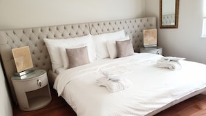 Un lit bien fait, avec du linge de lit blanc, deux tables de chevet avec des lampes et un grand miroir au mur.