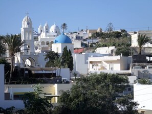 A coastal town with white buildings, blue domes, and palm trees. - Santorious Apartments (Santorini)