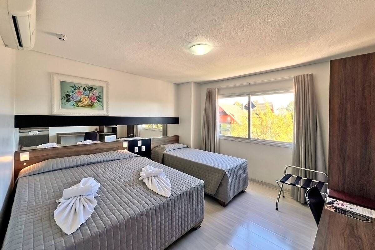 A hotel room with two beds, a desk, a chair, a window with curtains, and a painting on the wall.