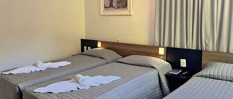 A hotel room with two beds, each with a quilted bedspread and rolled towels. There is a framed picture on the wall and a nightstand with a phone and a lamp.