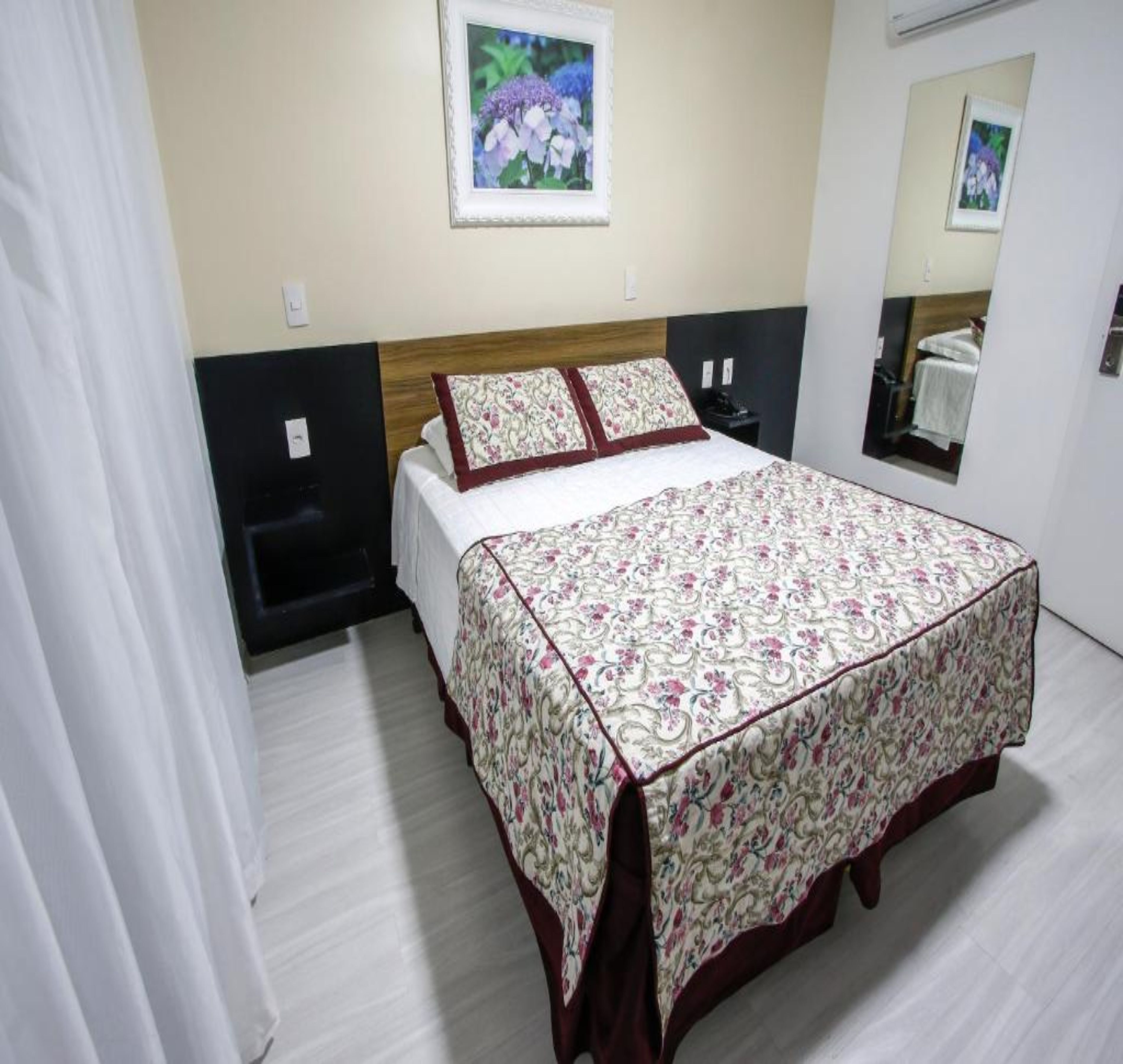 A neatly made bed with a floral bedspread, a headboard, and a wall-mounted picture.