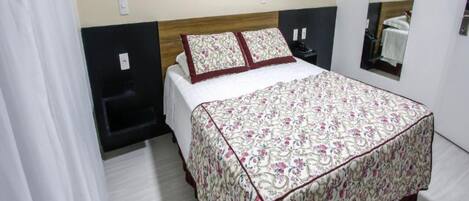 A neatly made bed with a floral bedspread, a headboard, and a wall-mounted picture.