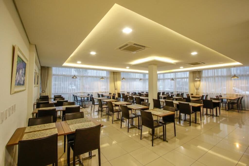 Un comedor amplio con varias mesas y sillas, ventanas grandes con cortinas e iluminación empotrada en el techo.