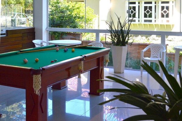 A pool table with balls, surrounded by white chairs and a potted plant.
