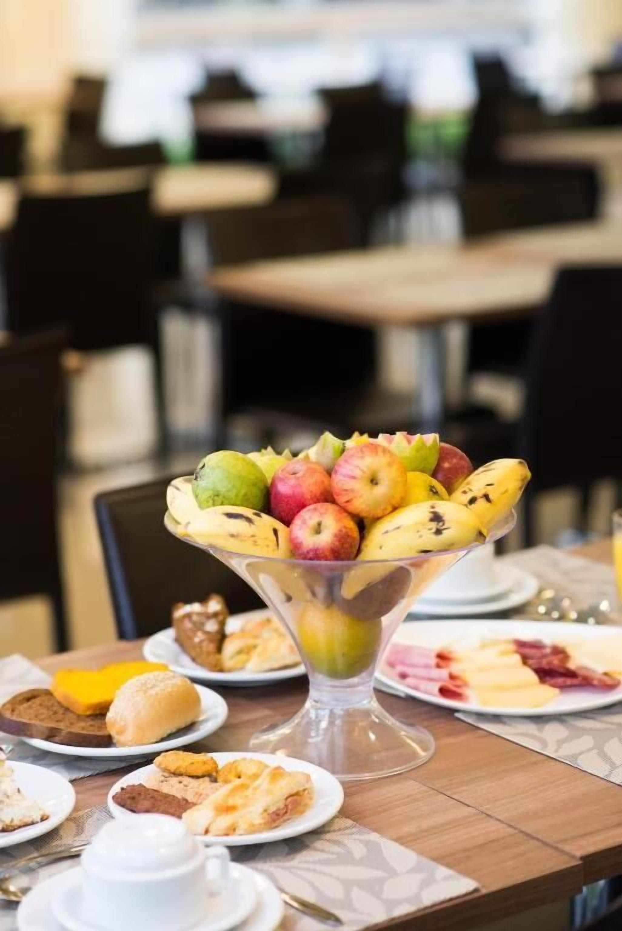 Una mesa de comedor con diversos productos para el desayuno, incluyendo un bol de fruta, pastelería y una taza.