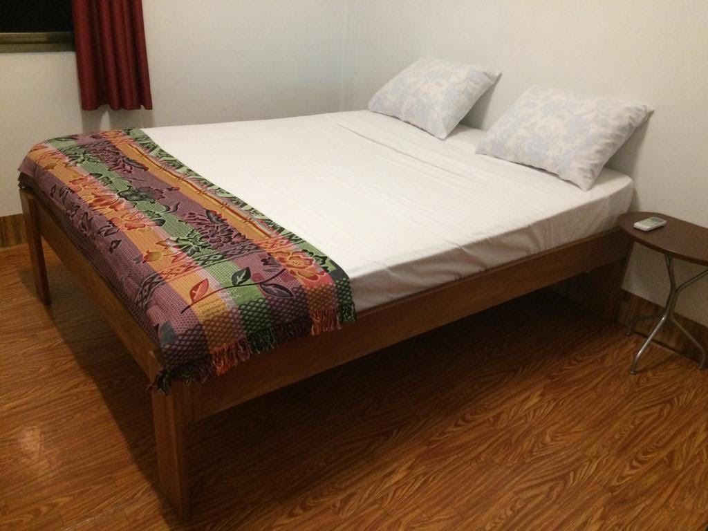 A single bed with a colorful blanket and two pillows, a small table, and a wooden floor.
