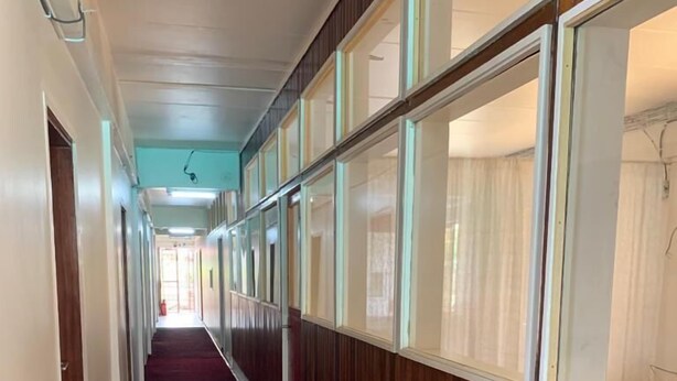 A long hallway with wooden paneling and large windows on one side, leading to a bright room at the end. - Hotel Midnight (Paramaribo)