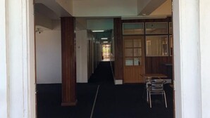 A hallway with a carpeted floor, wooden columns, and a table with chairs in the distance. - Hotel Midnight (Paramaribo)