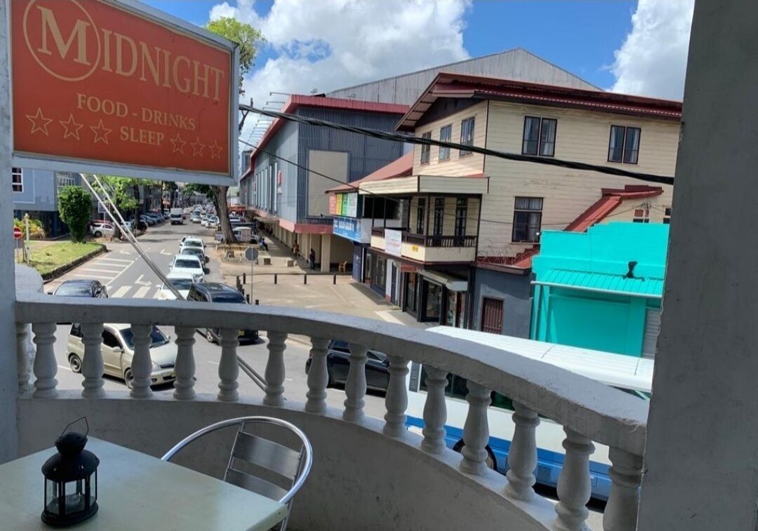 A balcony with a view of a street, a sign for 'Midnight Food-Drinks Sleep', and a building with a red roof.