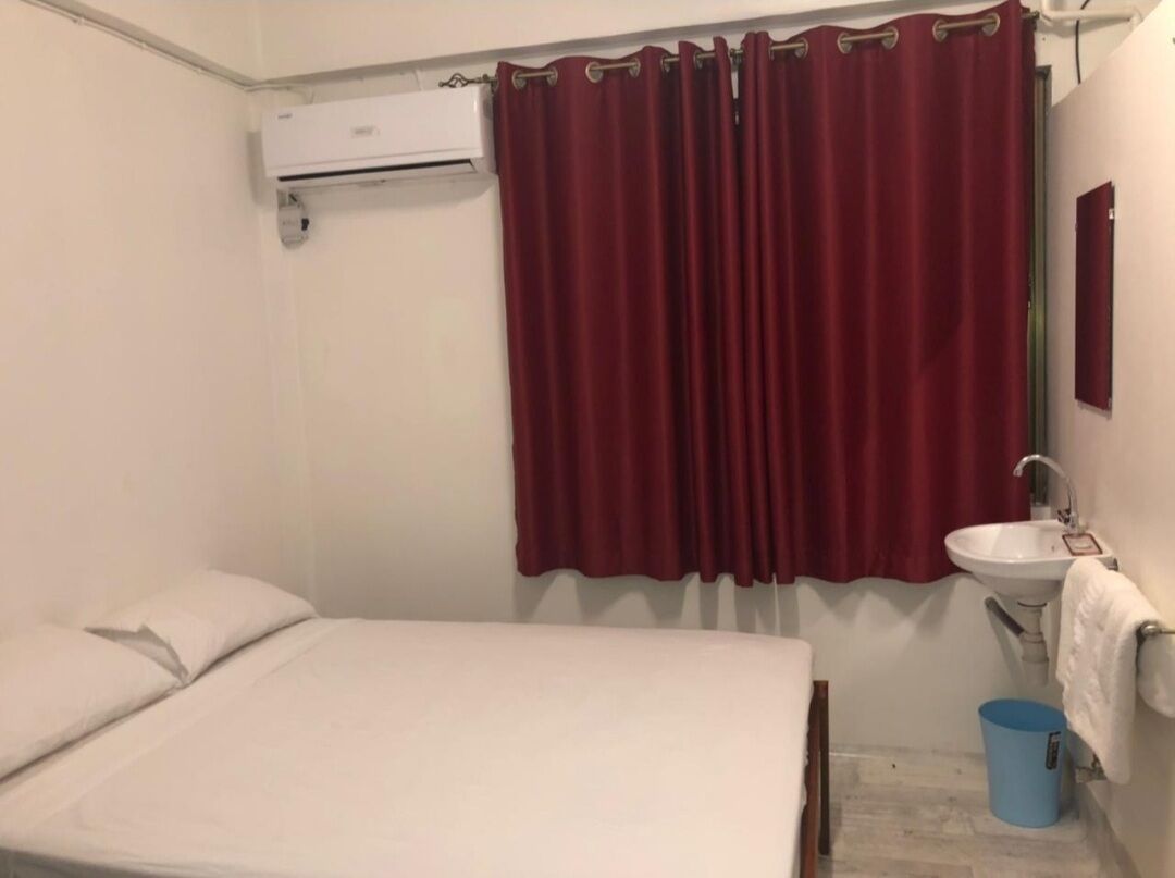 Une chambre à coucher avec un lit, un lavabo blanc et une poubelle bleue.