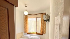 A small, cozy bedroom with a single bed, a bedside table, a window with curtains, and a wall-mounted light fixture. - Uysal Pansiyon (Bozcaada)