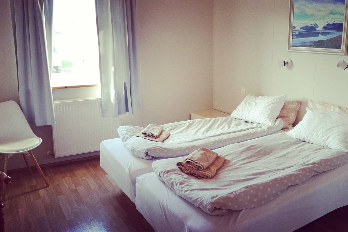A room with two beds, a chair, and a window with curtains.