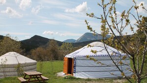 Una yurta con una mesa de picnic en un campo cubierto de hierba, rodeada de montañas y árboles.