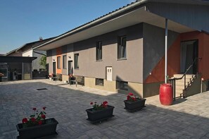 A modern building with a flat roof, large windows, and a covered outdoor area with potted plants. - Apartments Drevi (Ljubljana)