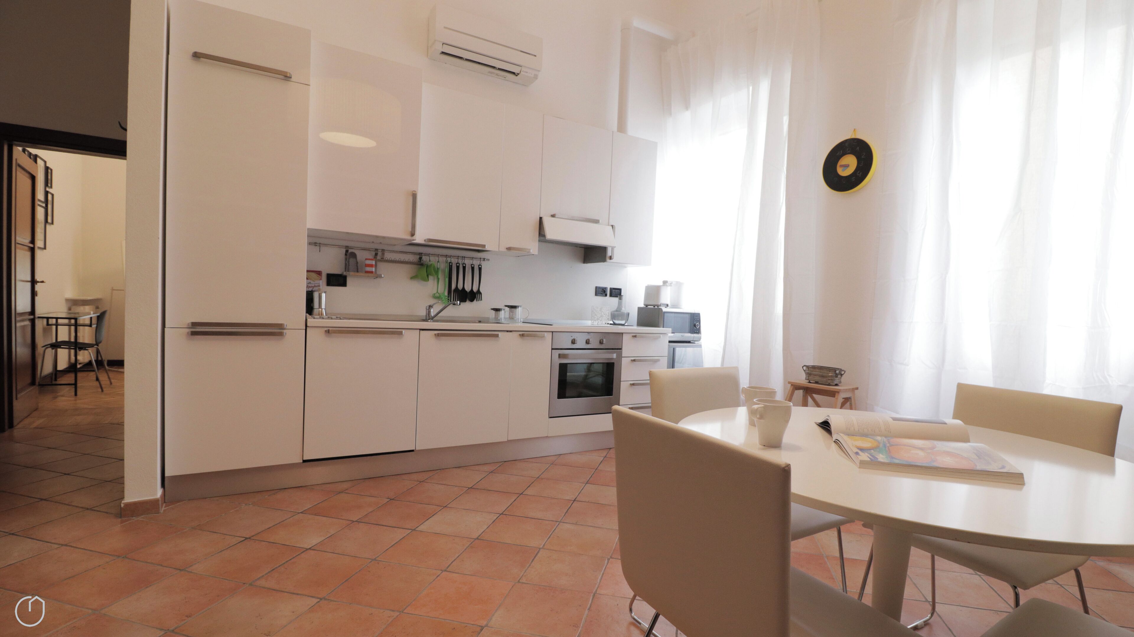 Une cuisine moderne avec des meubles blancs, un four encastré et un coin repas comprenant une table ronde et des chaises.