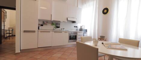 Une cuisine moderne avec des meubles blancs, un four encastré et un coin repas comprenant une table ronde et des chaises.