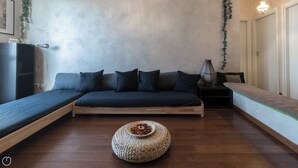 A modern room with a built-in sofa, a round woven ottoman, and a small table with a decorative item. - Italianway - Pichi 19 (Milan)