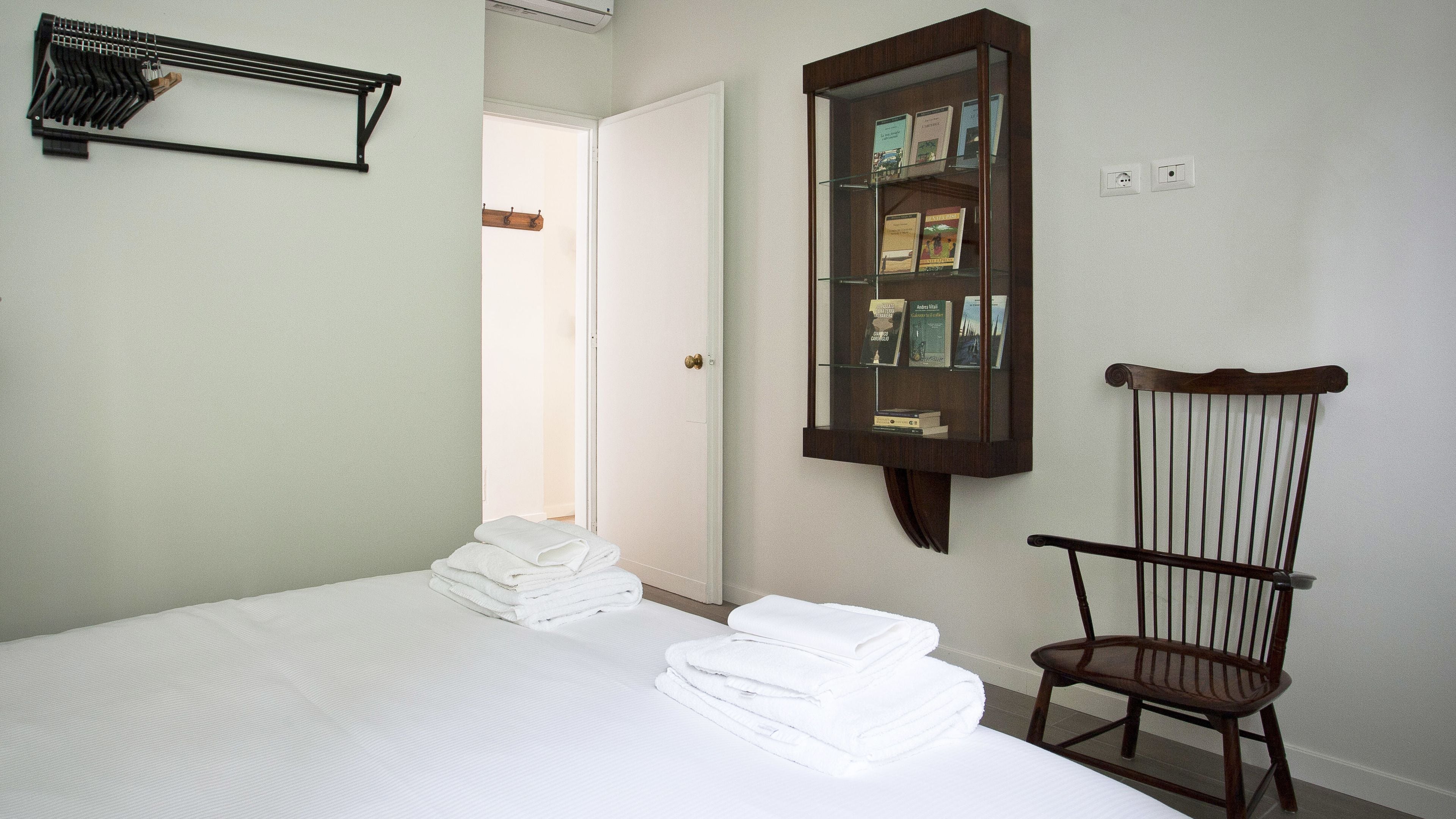 Een slaapkamer met een bed, een houten stoel, een spiegel en een deur.
