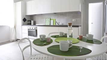 Una cocina moderna con armarios blancos, un horno de acero inoxidable y una mesa de comedor con posavasos verdes y tazas blancas.