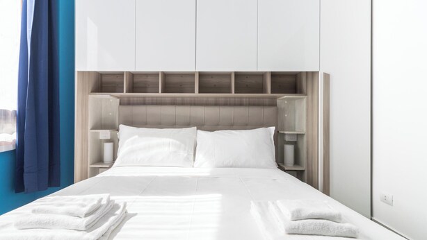 Ein modernes Hotelzimmer mit einem großen Bett, einem Holz-Kopfteil, weißen Bettwäsche und einem blauen Vorhang.