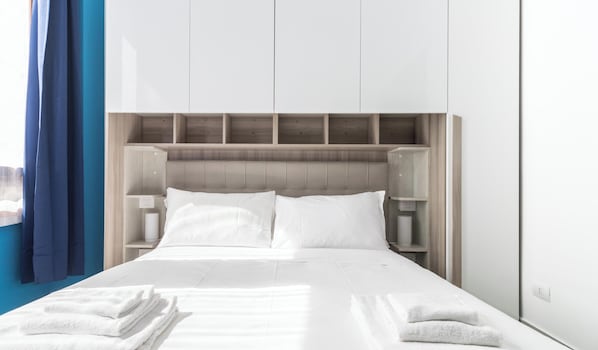 A modern hotel room with a large bed, wooden headboard, white linens, and a blue curtain.