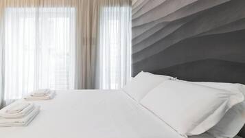 Una habitación de hotel con cama, escritorio y vistas al exterior a través de cortinas translúcidas.