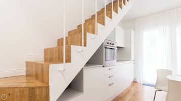 Una cocina moderna con armarios blancos, horno empotrado y escalera de madera.