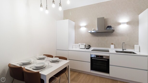 A modern kitchen with white cabinetry, a built-in oven, a stainless steel range hood, and a countertop with a kettle and toaster. - Italianway Easy - Vigevano 13 (Milan)