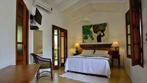 Un dormitorio con cama, una silla, una mesa, un cuadro y televisor.