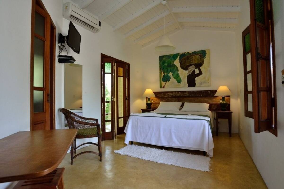 A bedroom with a bed, a chair, a table, a painting, and a television.
