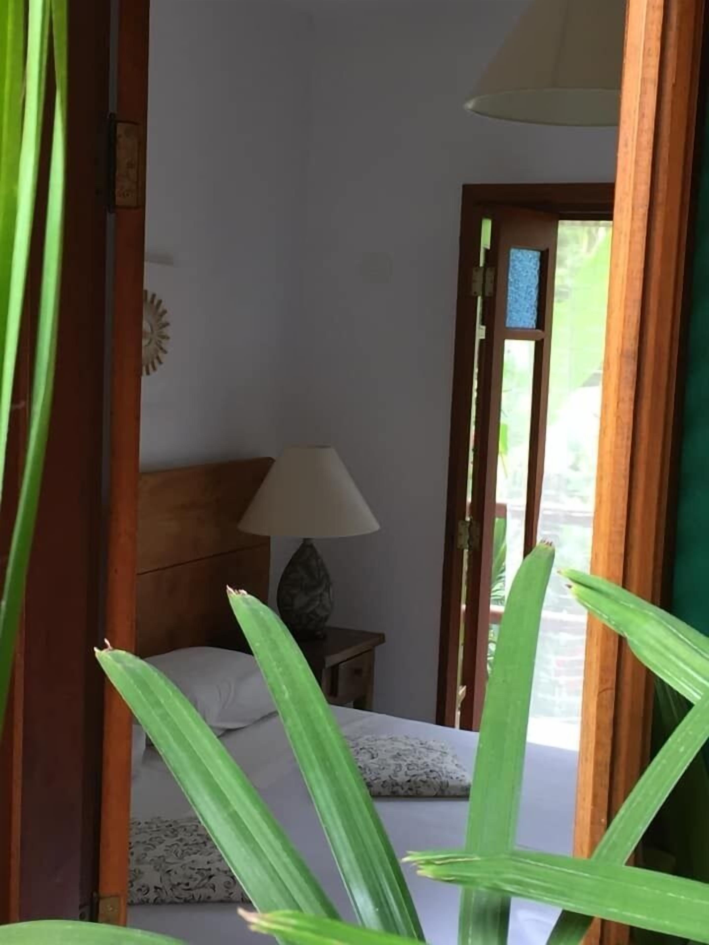 A room with a bed, a nightstand with a lamp, and a view through a doorway.