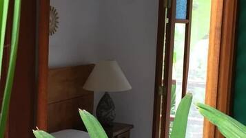 A room with a bed, a nightstand with a lamp, and a view through a doorway.