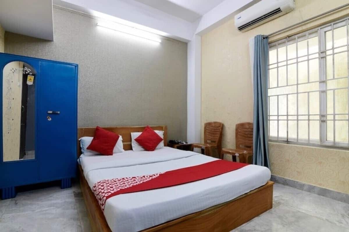 A hotel room with a large bed, a wardrobe, a desk, and a window with bars.