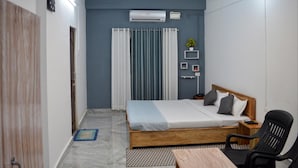 A bedroom with a bed, a desk, a chair, a ceiling fan, and a window with curtains. - Hotel Value (Port Blair)