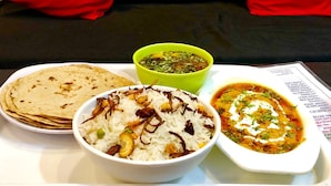 A table with a meal consisting of rice, a bowl of soup, and a bowl of curry, set against a black couch with red cushions. - Hotel Value (Port Blair)