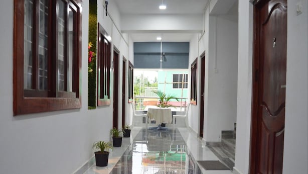 A hallway with a shiny tiled floor, potted plants, and doors leading to rooms. - Hotel Value (Port Blair)