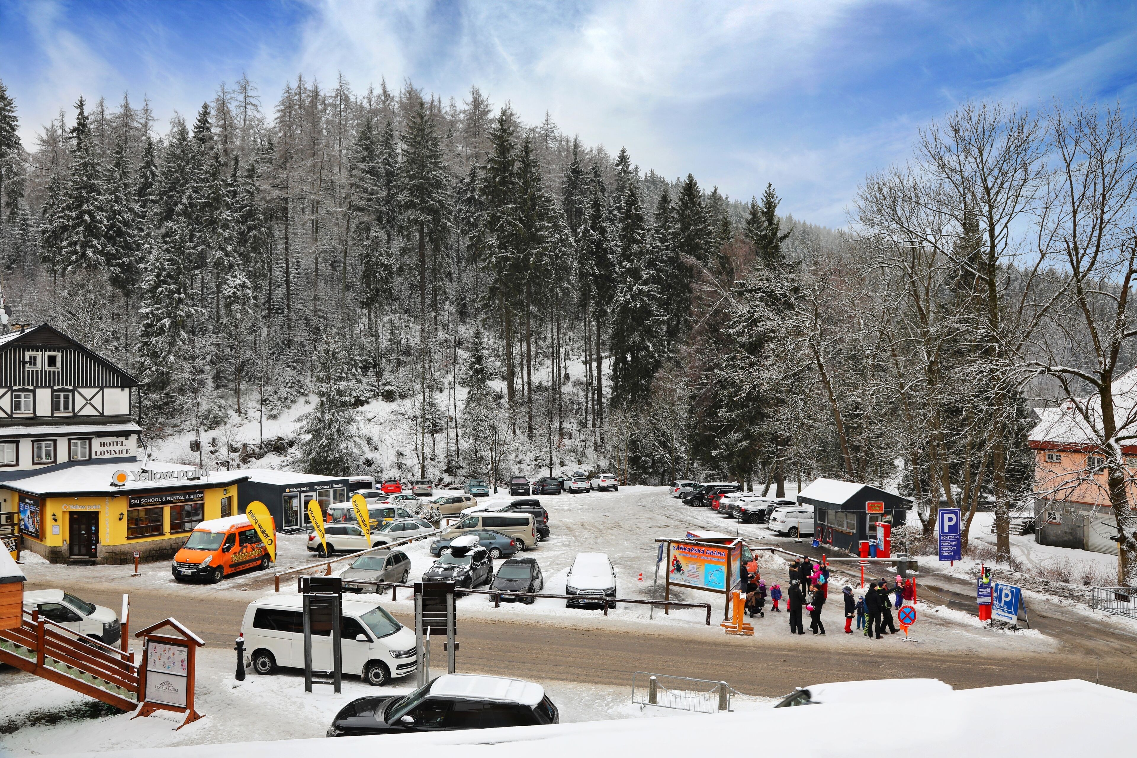 A hotel with a signboard, a parking area, and a snowy forest in the background.