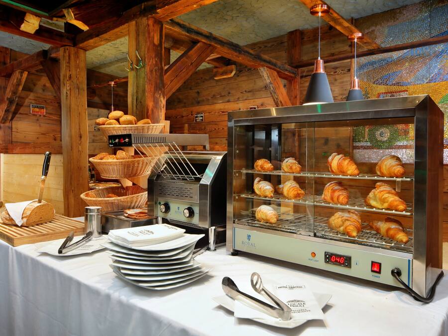 A bakery setup with a display case of croissants, a bread slicer, and a basket of bread on a table.