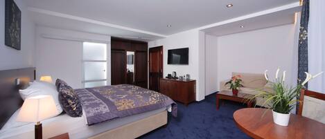 A hotel room with a bed, a desk, a chair, a TV, and a potted plant.