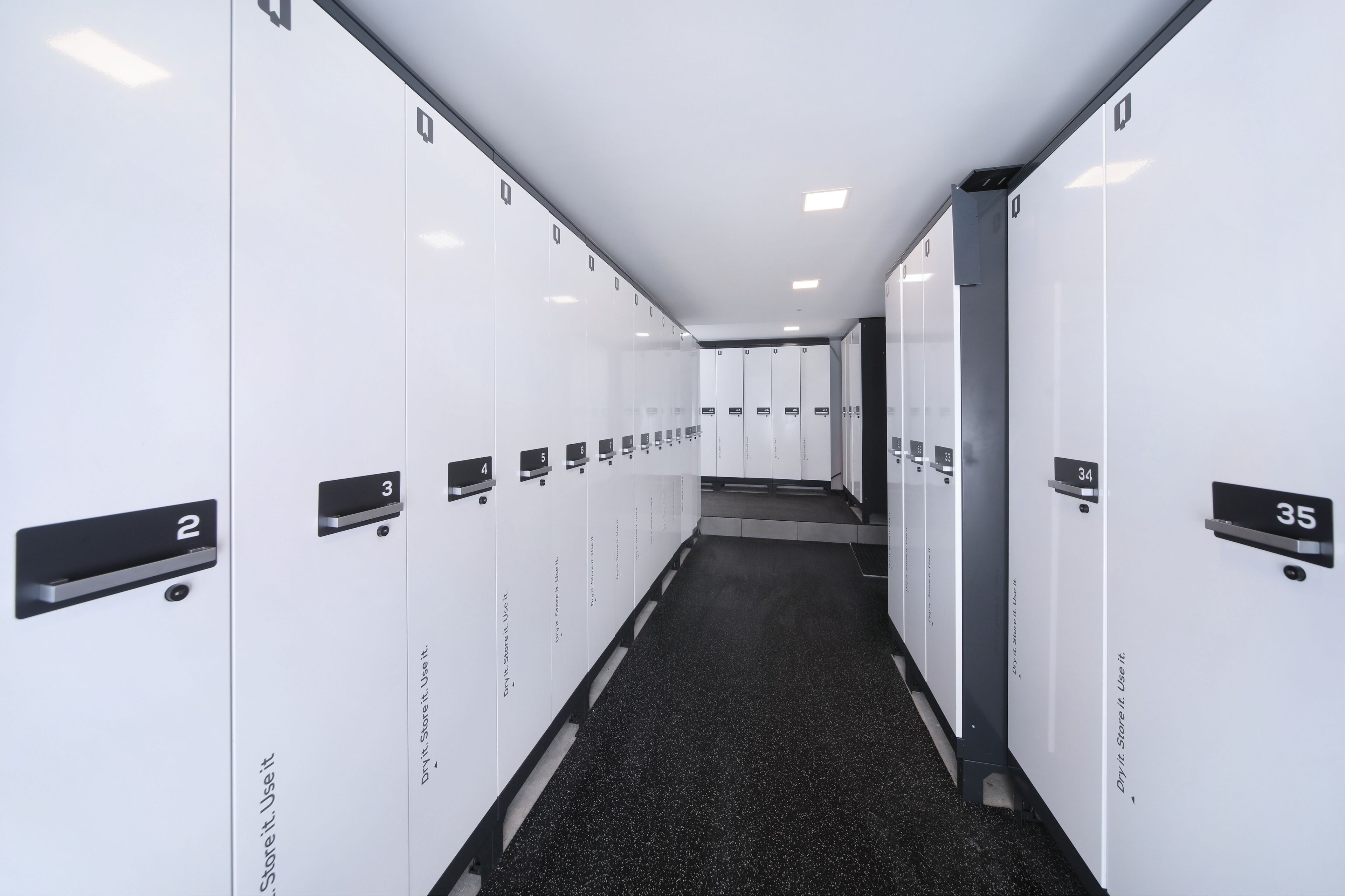 A hotel corridor with lockers numbered 2 to 35, a tiled floor, and a clean, modern design.