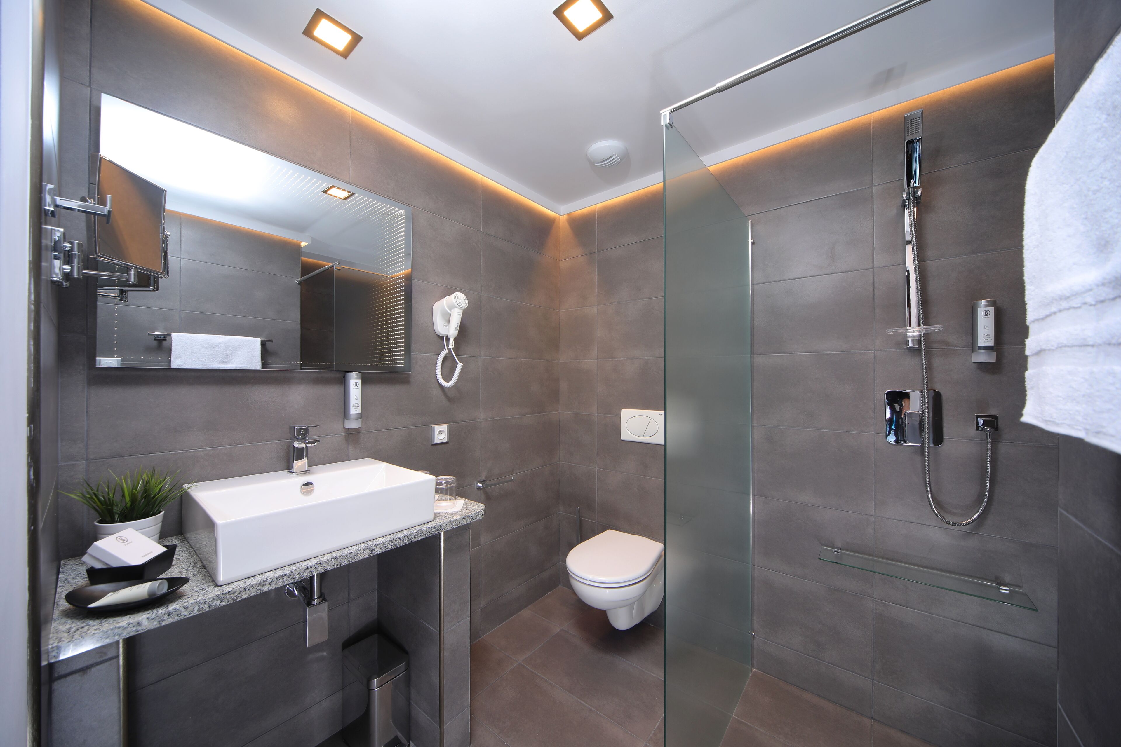 Un baño moderno con un espejo grande, un lavabo blanco, cabina de ducha con mampara de vidrio y un inodoro.