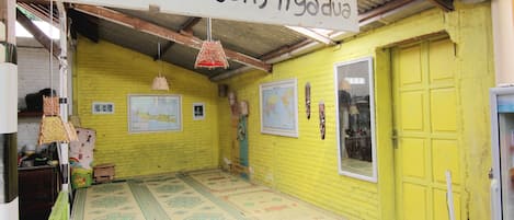 A room with a yellow wall, a wooden door, and a sign reading "Balai Bengong Tigo dua".