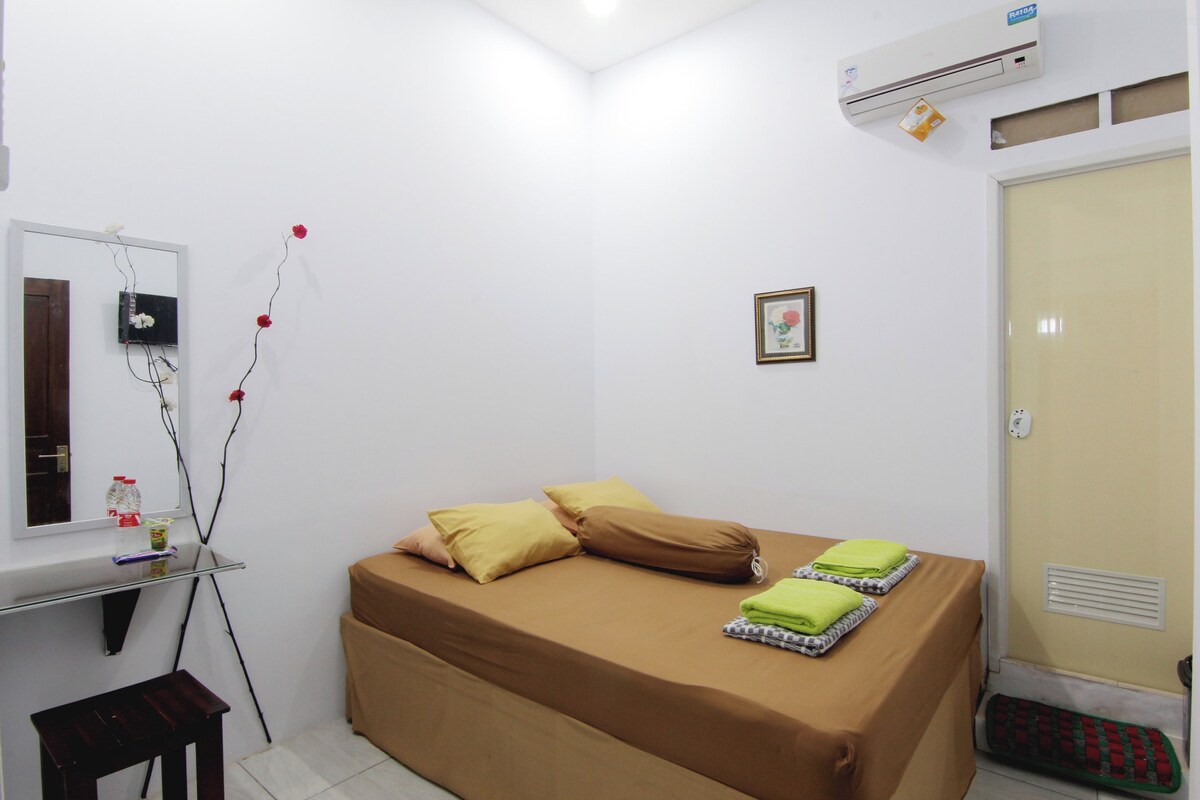 A small, clean room with a bed, a mirror, a small table, and a heater.