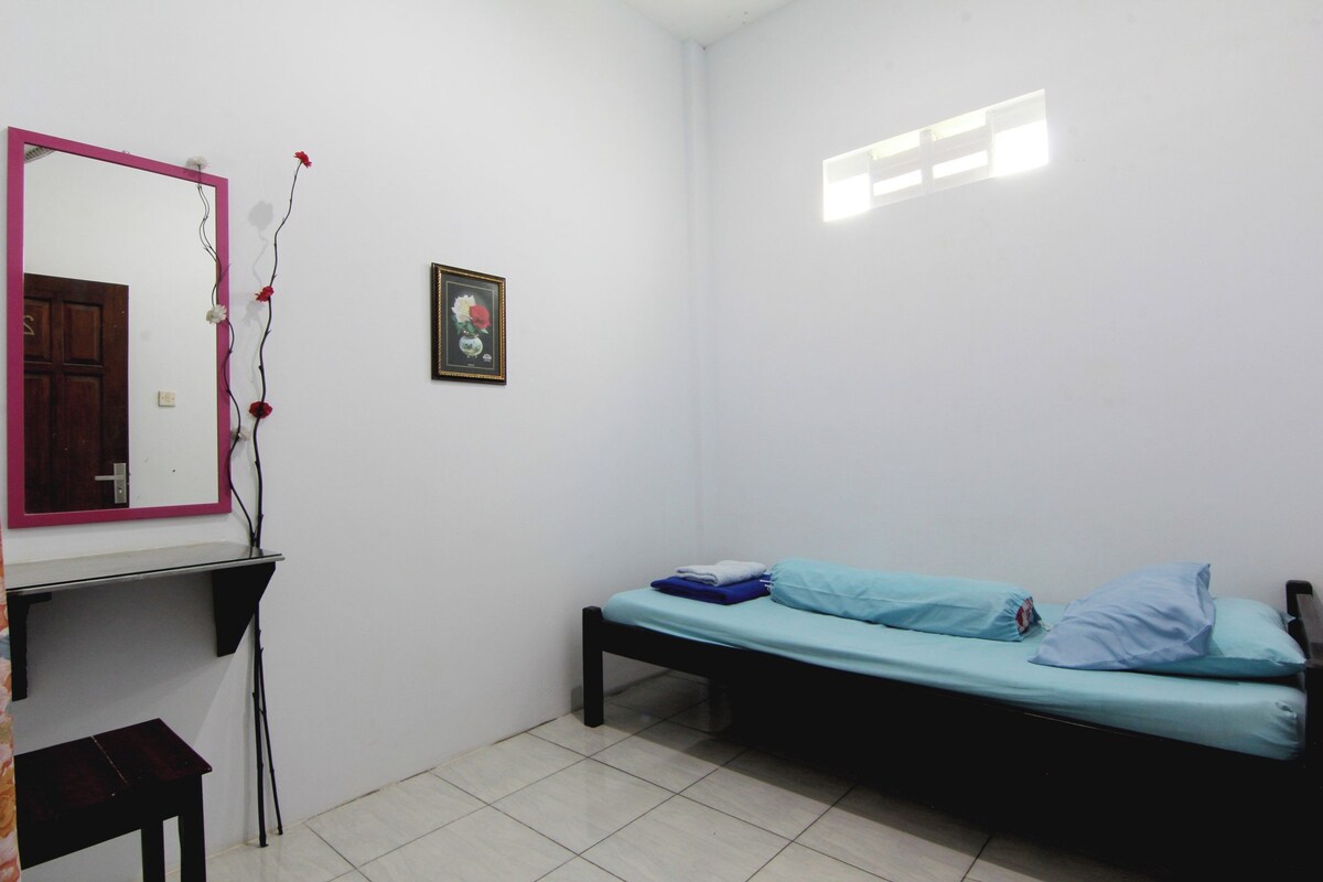 A small, sparsely furnished room with a bed, a desk, and a mirror.